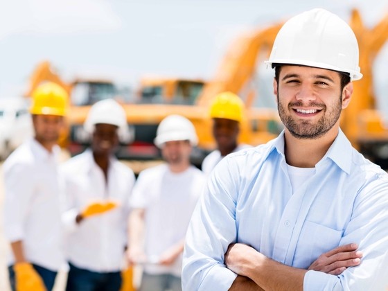 Architekt auf einer Baustelle mit Projektteam und Baumaschinen im Hintergrund