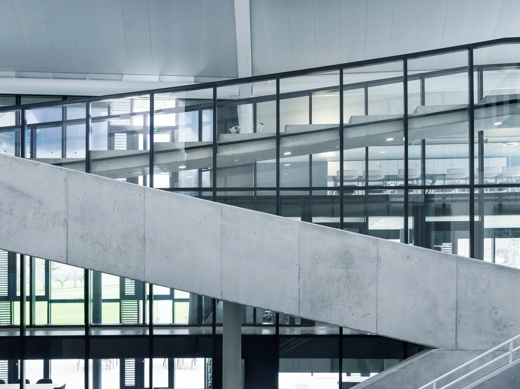 Modernes Gebäudeinnere mit Glasfassaden und schräg verlaufenden Betonrampen