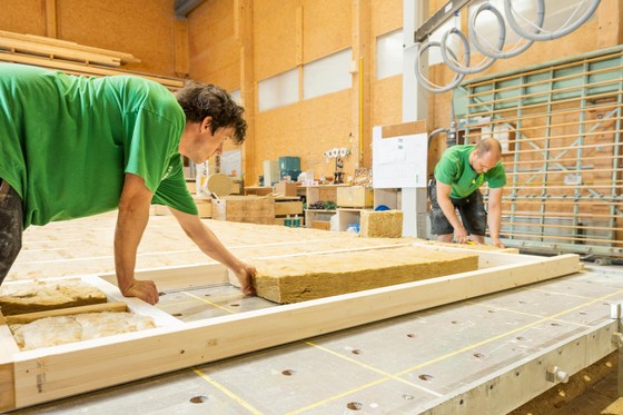 Deux employés installent un matériau isolant dans une structure en bois dans une salle d'usine