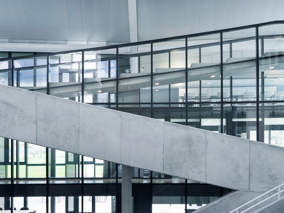 Modernes Gebäudeinnere mit Glasfassaden und schräg verlaufenden Betonrampen